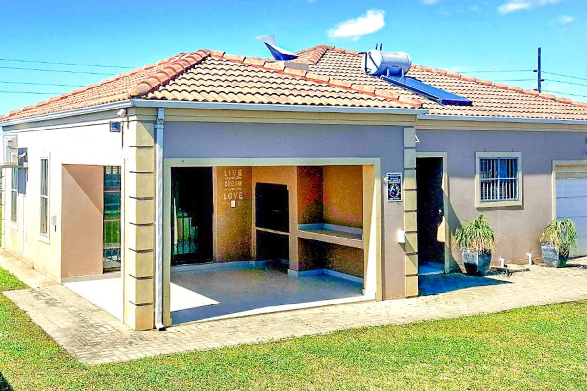 Rear view of the house featuring a covered patio with a built-in braai, tiled roof, and solar water heating system.
