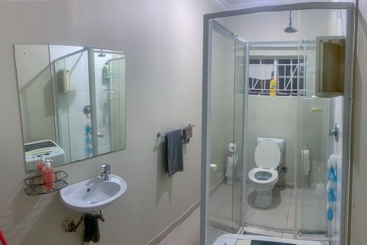 A functional bathroom featuring a wall-mounted basin, a glass-enclosed shower, and a standard toilet with tiled flooring.