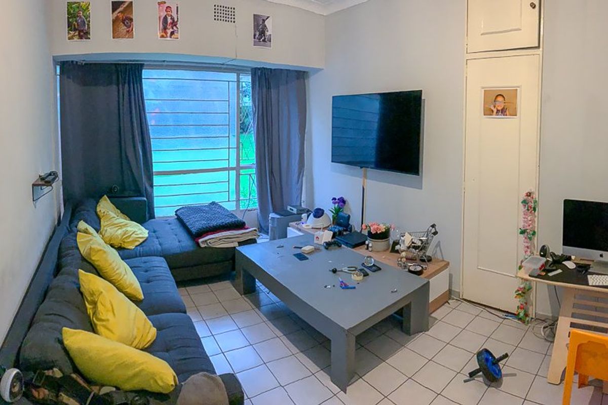 A living room featuring tiled flooring, a large window with security bars, and a built-in storage cupboard.