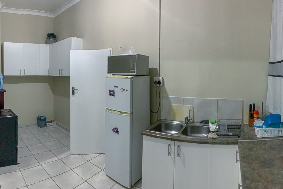 A functional kitchen area featuring white cabinetry, a double-basin sink, tiled flooring, and a dedicated space for a freestanding stove.