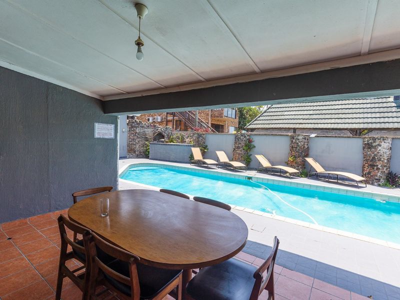 Covered patio area overlooking a swimming pool with a stone-clad boundary wall and built-in outdoor braai facility.
