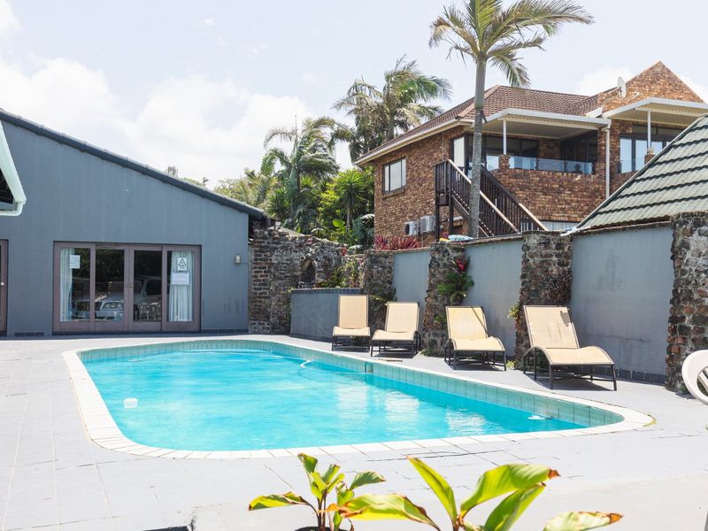 Outdoor pool area featuring a tiled deck, stone-clad boundary walls, and direct access to the main building via sliding glass doors.