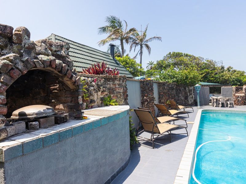 Outdoor pool area featuring a built-in brick barbecue, stone boundary wall, and tiled deck space, ideal for outdoor entertaining.