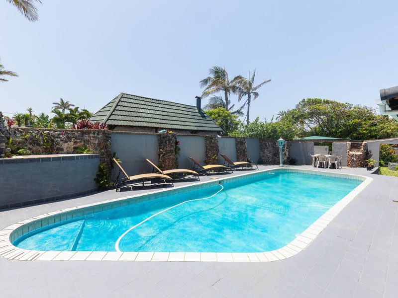 Outdoor pool area featuring a tiled deck, stone-clad boundary walls, and a built-in brick braai, perfect for entertaining.