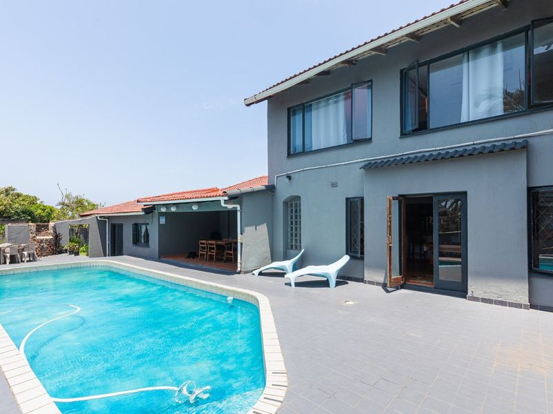 A spacious rear exterior featuring a swimming pool, tiled patio area, and a covered outdoor entertainment space attached to the main residence.