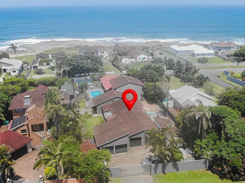 Aerial view of a coastal residential property featuring a tiled roof, double garage, and paved driveway, situated in a prime seaside location.