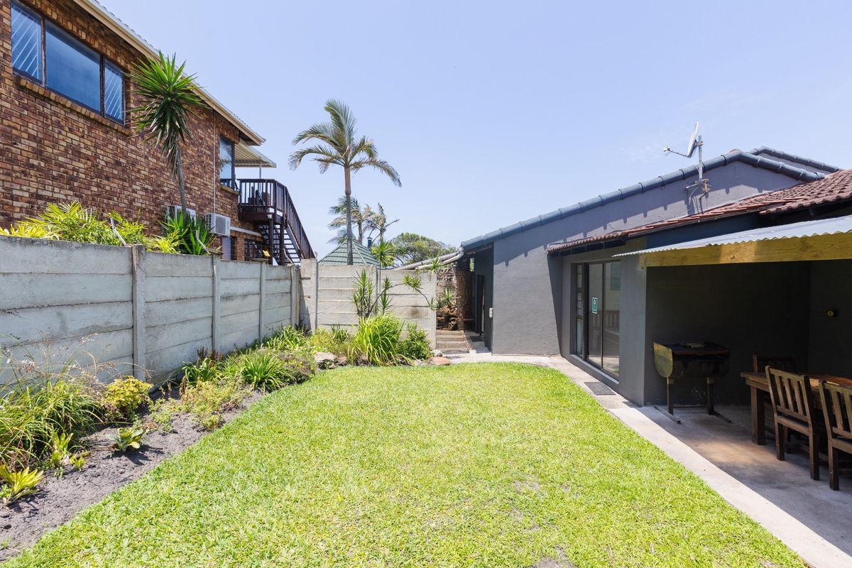 A private rear garden featuring a lawn, landscaped borders, and a covered patio area with direct access to the home via sliding doors.