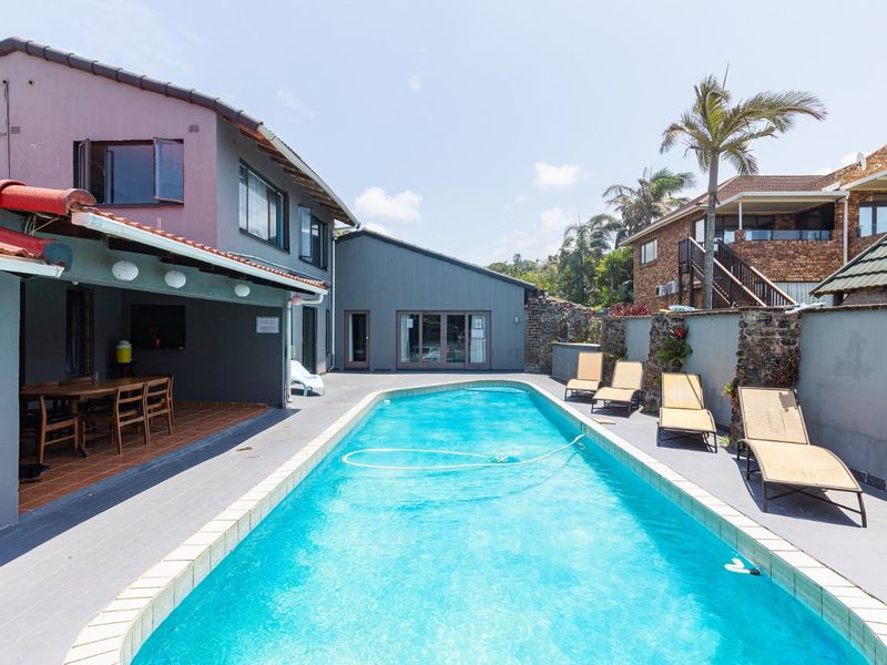 Outdoor pool area featuring a swimming pool with tiled surround, a covered patio space, and stone boundary walls.