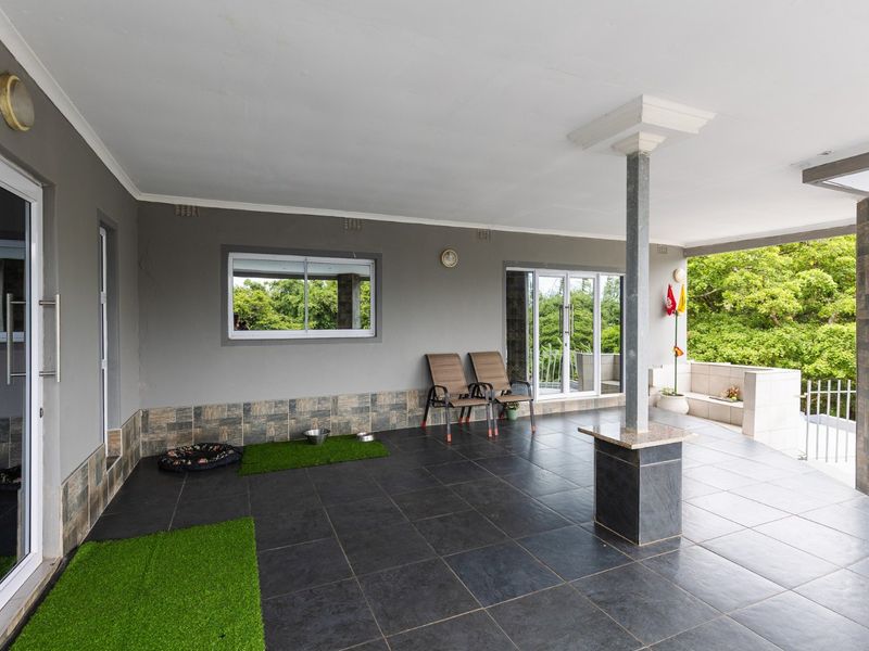 A spacious covered patio featuring dark tiled flooring, stone-clad wall accents, and sliding glass door access to the interior living areas.
