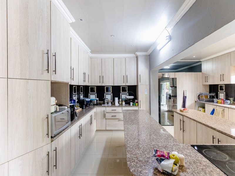 A spacious kitchen featuring extensive light wood-grain cabinetry, granite countertops, and a long central island with an integrated electric hob.