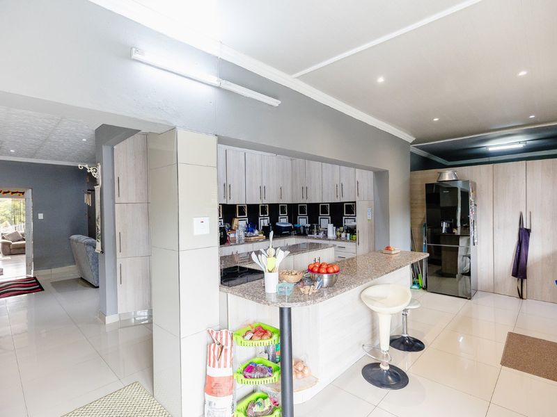 Open-plan kitchen featuring light wood-finish cabinetry, granite countertops, a breakfast bar, and tiled flooring, seamlessly connecting to the adjacent living area.