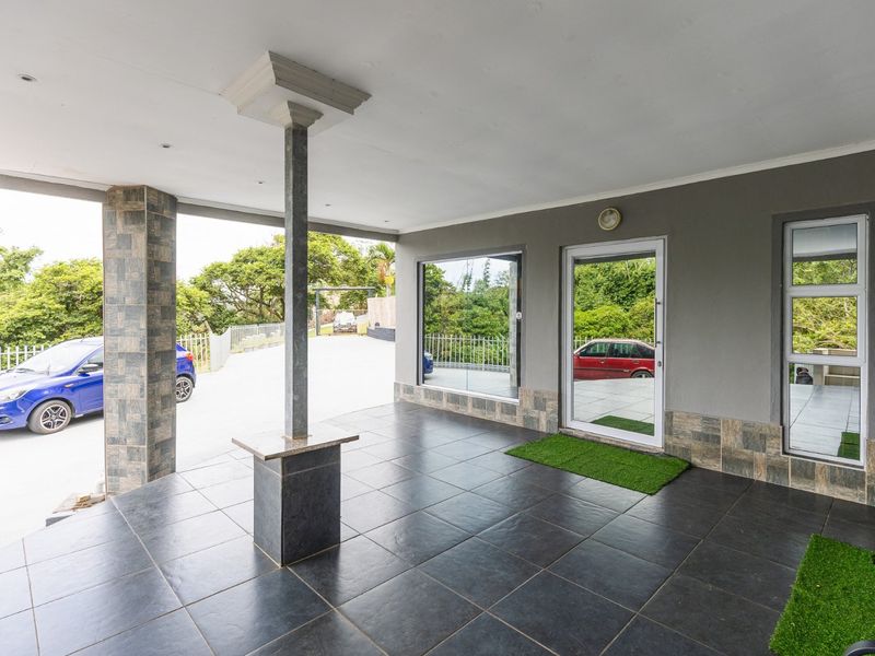 A spacious covered patio featuring dark tiled flooring, stone-clad support columns, and large glass doors providing access to the home.