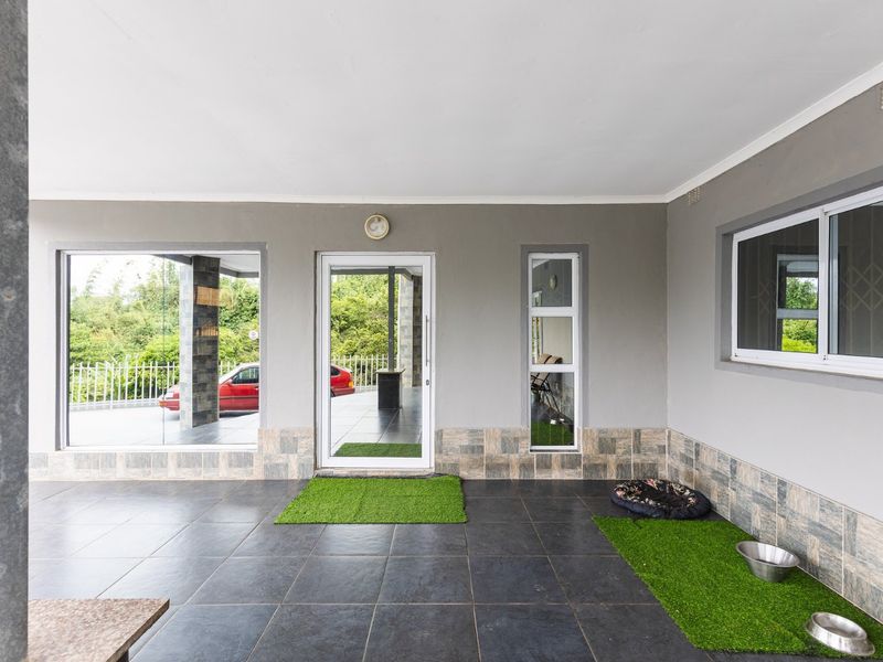 A covered patio area featuring dark tiled flooring, sliding glass doors, and large windows, providing a clean and functional outdoor living space.