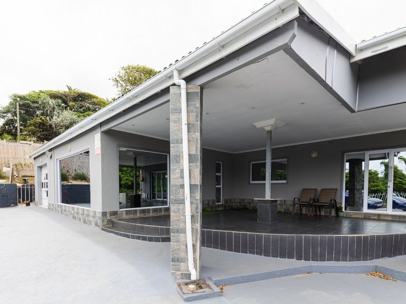 Spacious covered patio area featuring tiled flooring, stone-clad pillars, and large sliding glass doors providing seamless access to the interior living space.