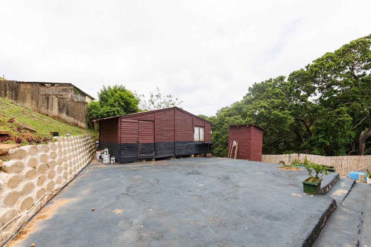 Rear outdoor area featuring a large concrete paved space, a timber storage shed, and a concrete block retaining wall.
