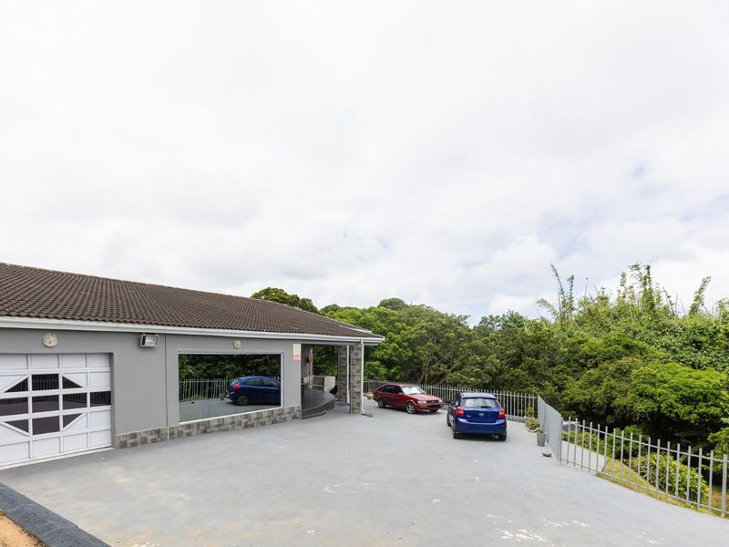 Front exterior view of the property featuring a paved driveway, garage access, and metal perimeter fencing surrounded by lush greenery.