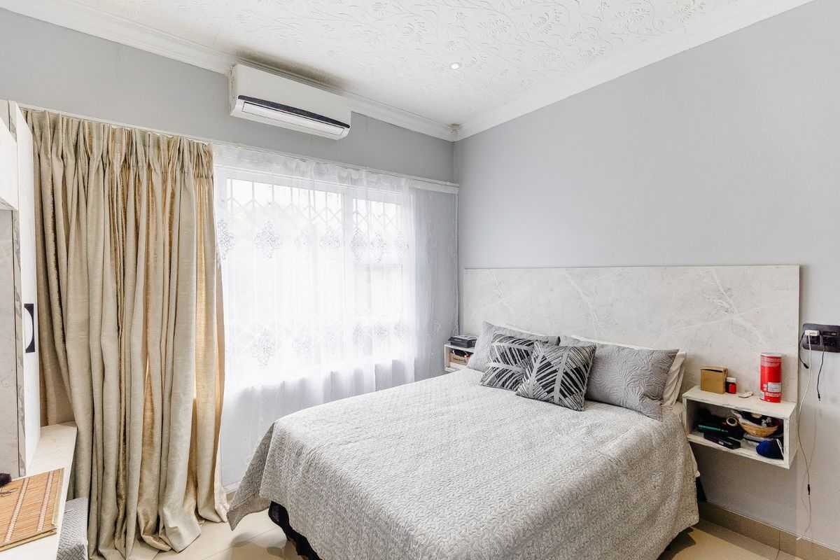 A well-maintained bedroom featuring a built-in headboard, floating bedside shelves, and a wall-mounted air conditioning unit.