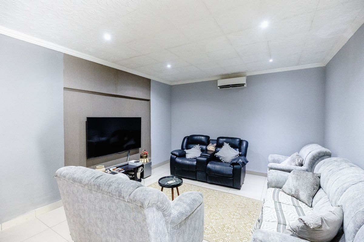 A comfortable living room featuring tiled flooring, a dedicated feature wall, recessed downlighting, and a wall-mounted split-system air conditioning unit.