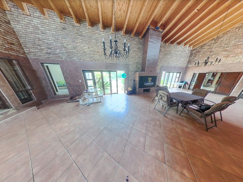 Spacious living area featuring high exposed timber beam ceilings, brick feature walls, tiled flooring, and a built-in fireplace with access to the garden.