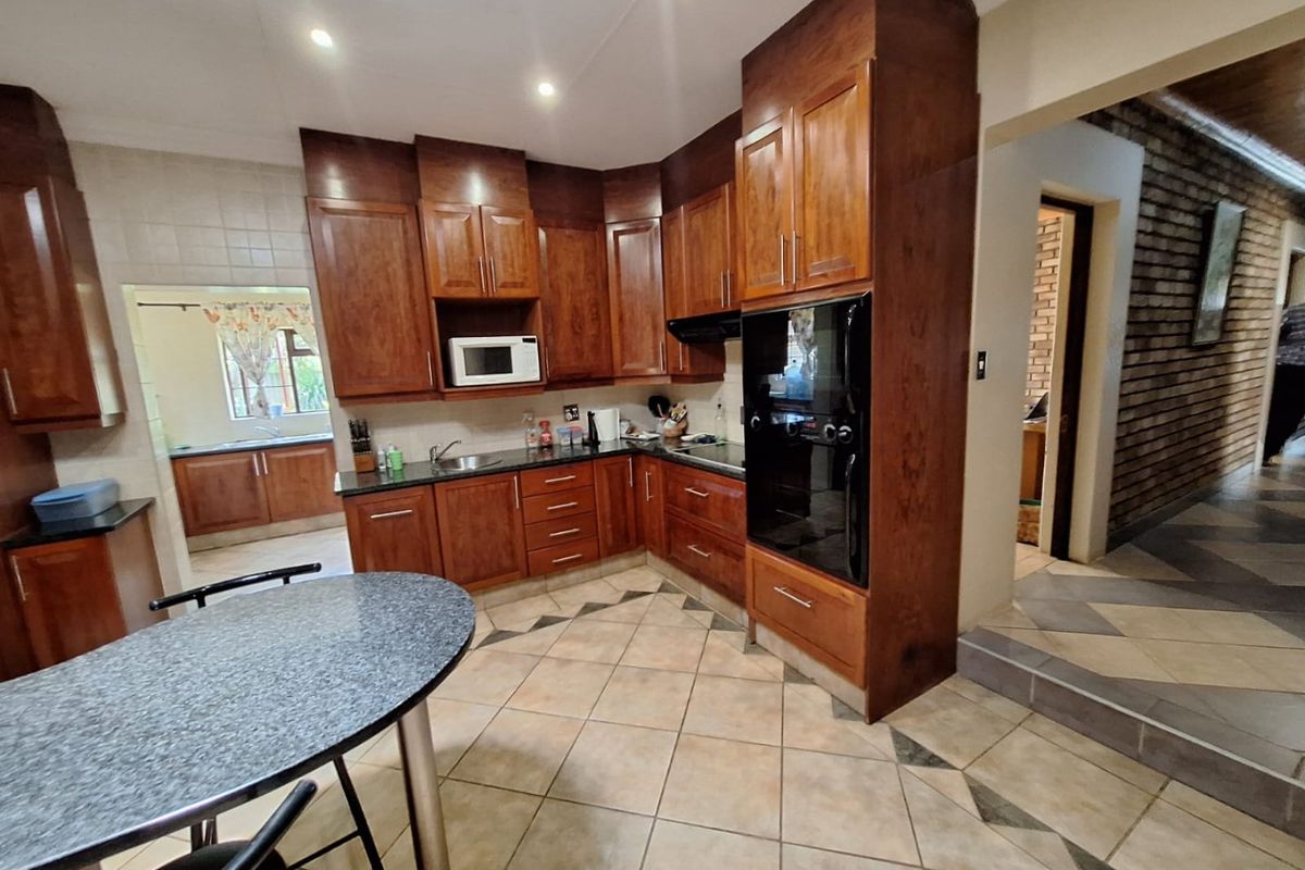 A functional kitchen featuring warm-toned wooden cabinetry, granite countertops, built-in oven, and tiled flooring, with an adjacent scullery area visible.