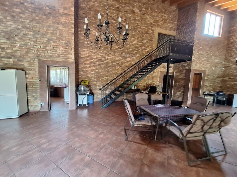 Spacious living area featuring double-volume exposed brick walls, tiled flooring, and a prominent metal staircase leading to an upper level.