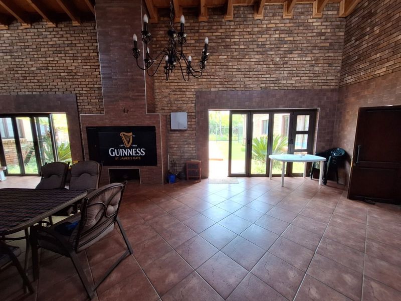 Spacious covered patio featuring exposed timber beams, a large brick fireplace, and tiled flooring with direct access to the garden through aluminium stacker doors.