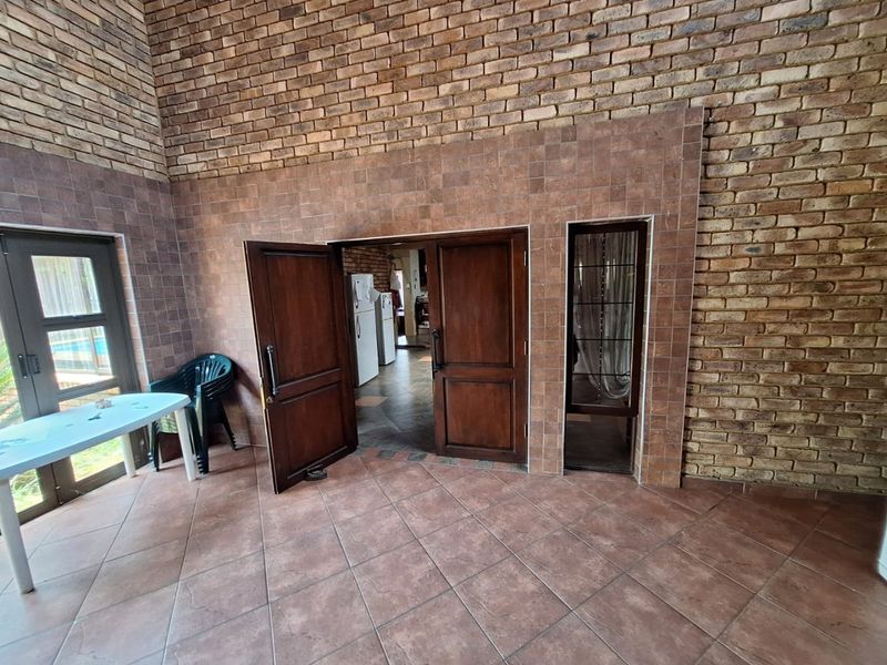 Covered patio area featuring exposed brick walls and tiled flooring, providing direct access to the interior living space through double wooden doors.