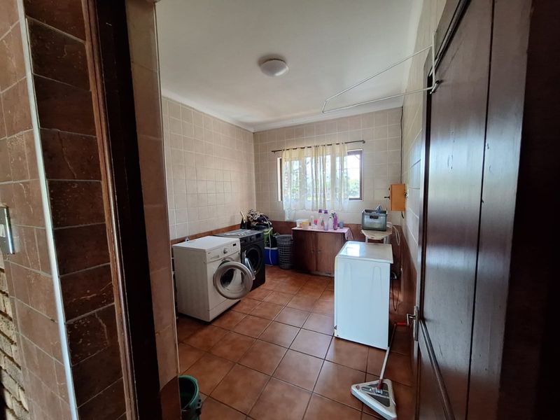 A functional laundry room featuring tiled walls and flooring, equipped with plumbing connections for washing machines and a wall-mounted drying rack.