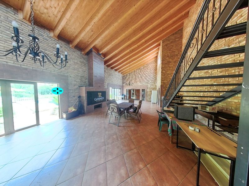 Spacious open-plan living area featuring high vaulted timber ceilings, exposed brick walls, a built-in fireplace, and a striking wrought iron staircase.