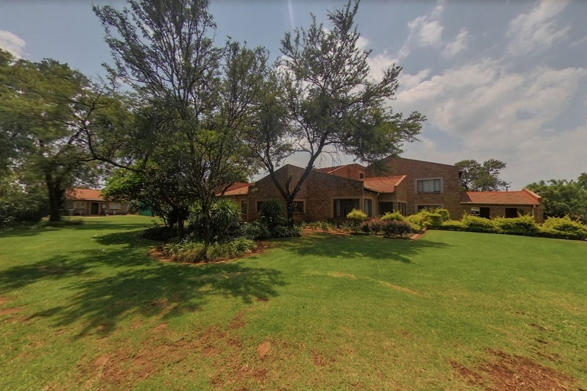 A spacious rear garden featuring a well-maintained lawn, mature trees, and a large brick-clad house with a traditional tiled roof.