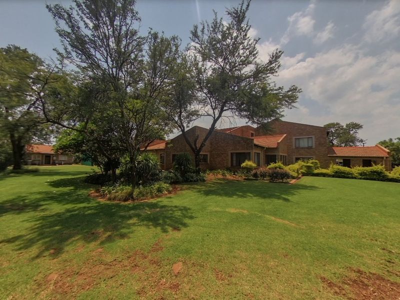 A spacious rear garden featuring a well-maintained lawn, mature trees, and a large brick-clad house with a traditional tiled roof.