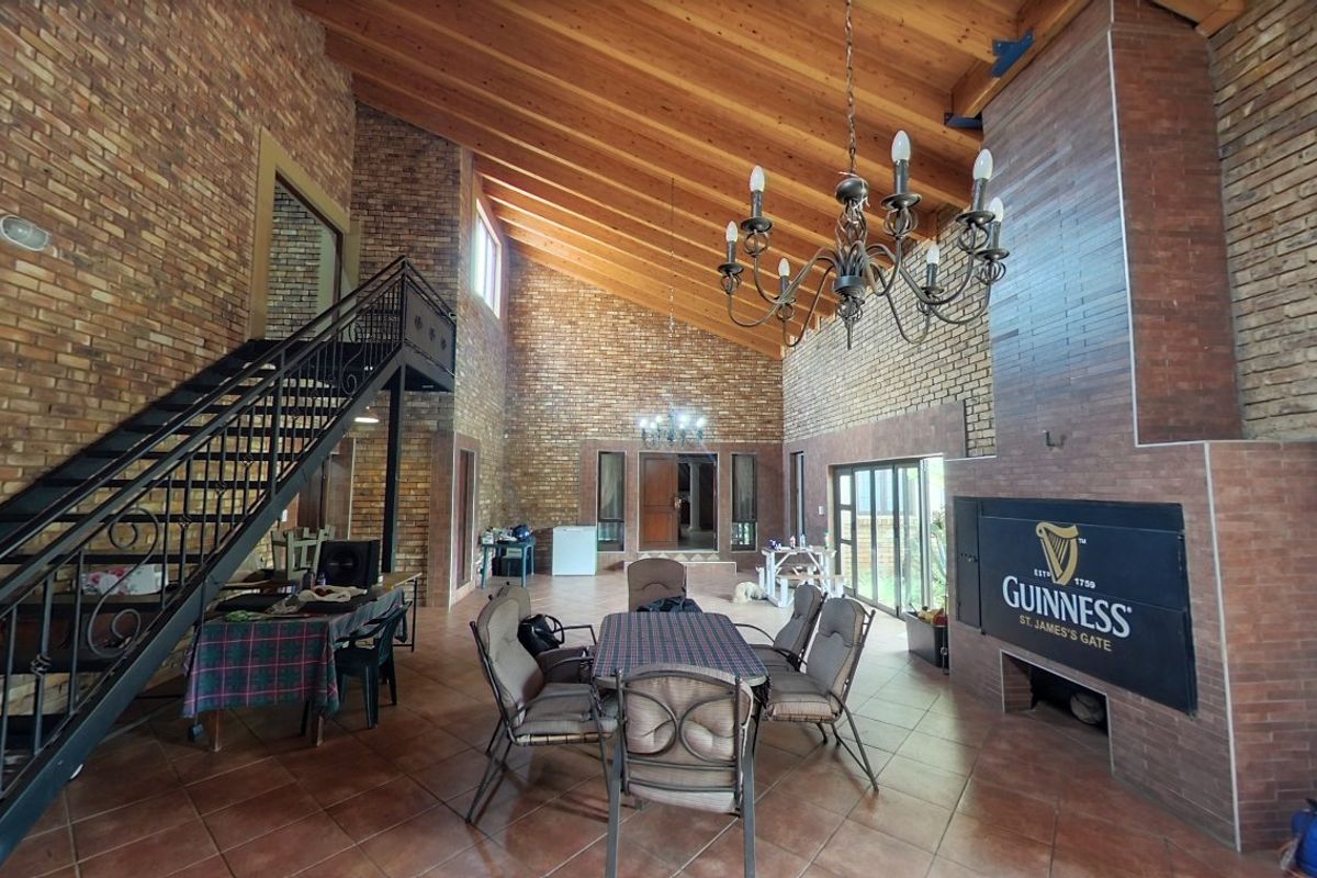 Spacious living area featuring high vaulted timber ceilings, exposed brick walls, a prominent built-in fireplace, and a wrought iron staircase leading to an upper level.