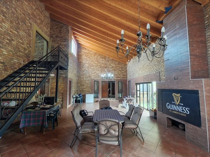 Spacious living area featuring high vaulted timber ceilings, exposed brick walls, a prominent built-in fireplace, and a wrought iron staircase leading to an upper level.