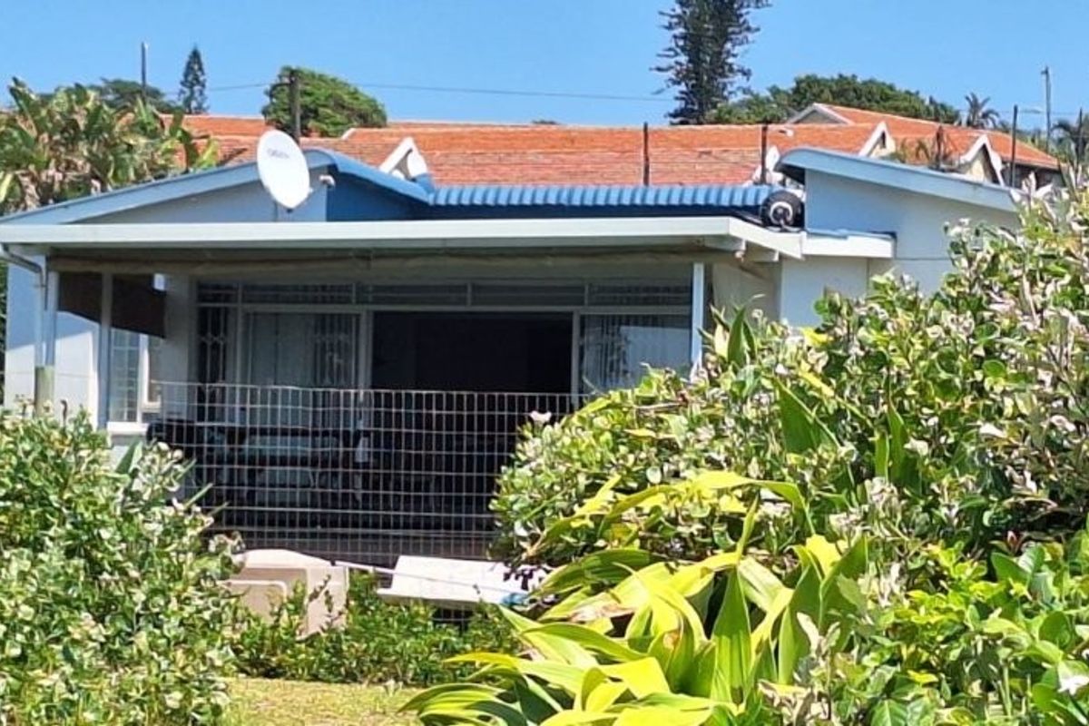 Rear view of a single-story house featuring a covered patio area, surrounded by established garden landscaping.