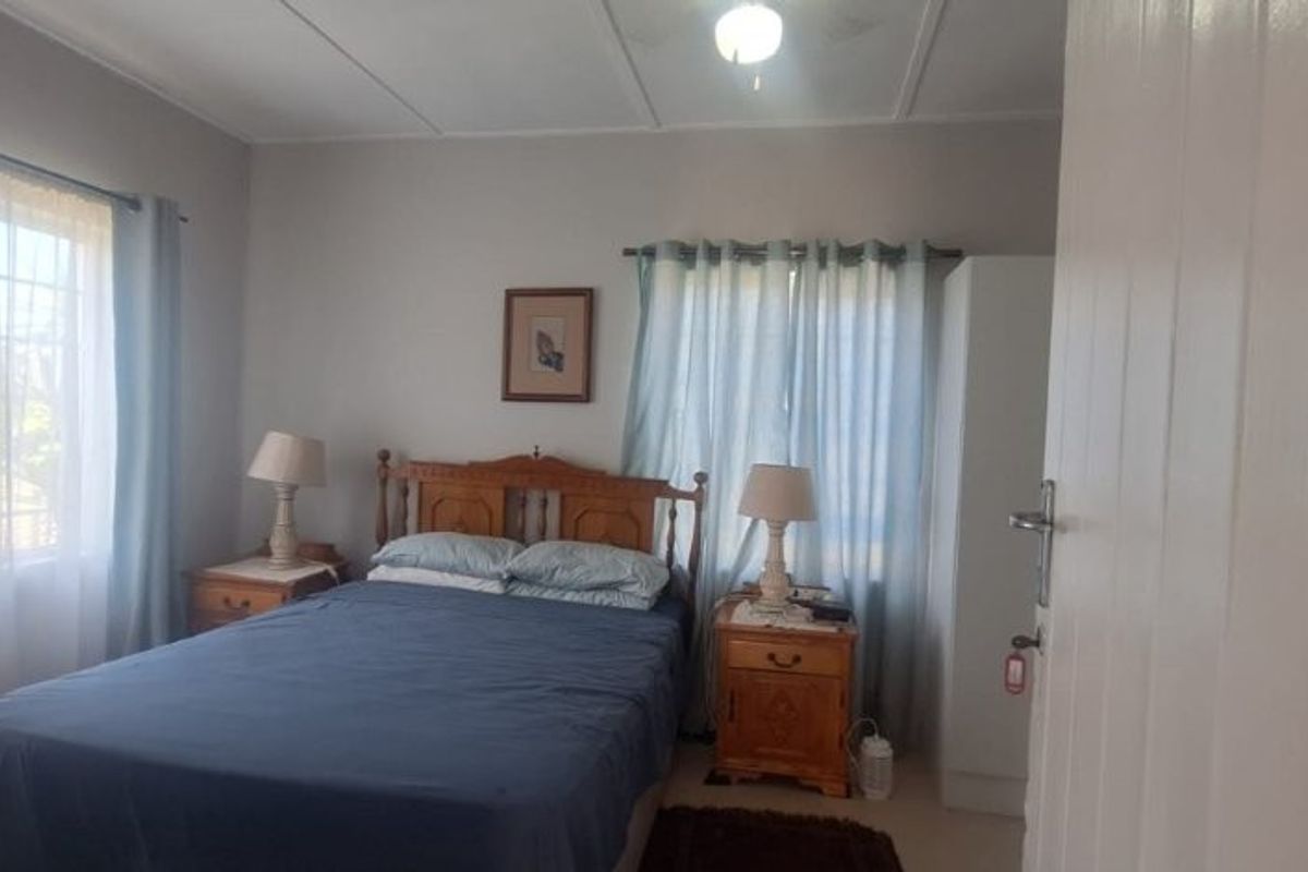 A functional bedroom featuring large windows with curtains, neutral wall finishes, and a standard ceiling light fixture.