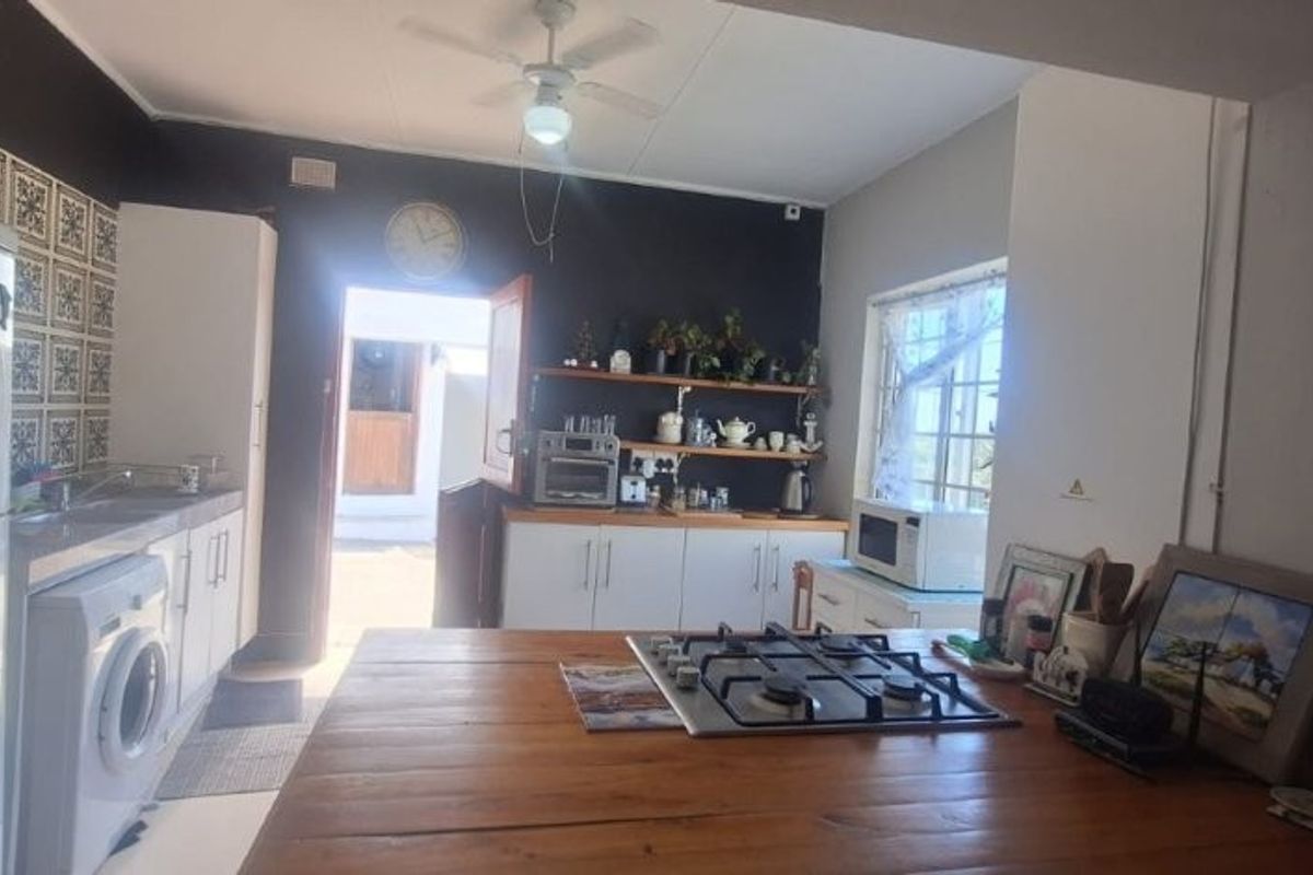 A functional kitchen featuring a central wooden island with a built-in gas hob, white cabinetry, and direct access to the exterior.