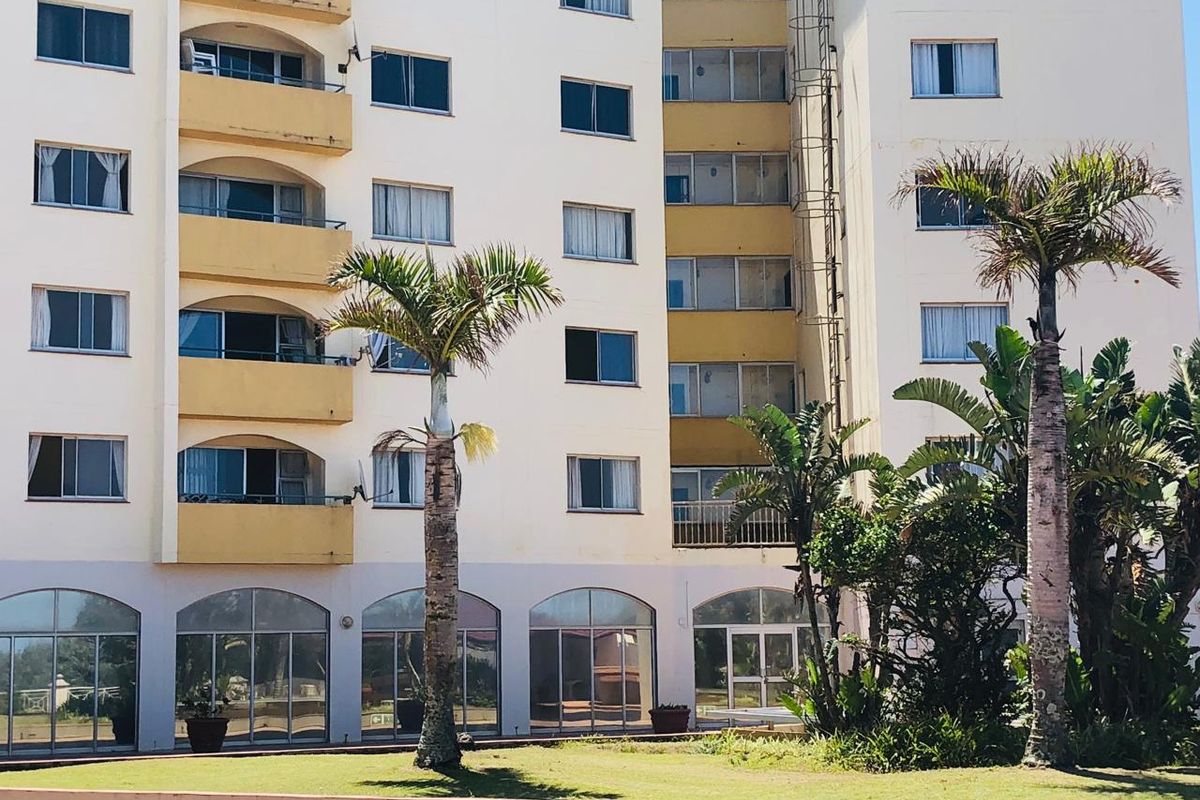 Exterior view of a multi-story apartment building featuring private balconies, arched ground-floor glass entrances, and established garden landscaping.