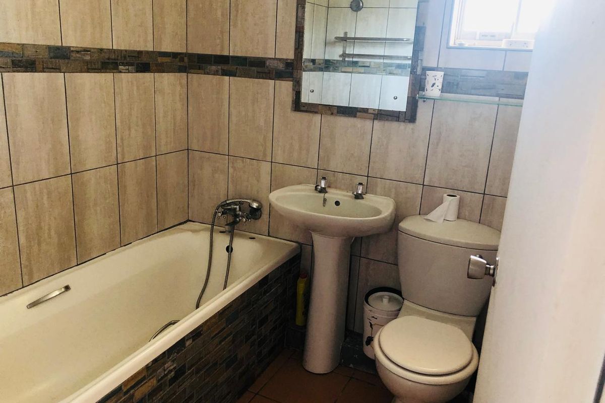 A functional bathroom featuring a bathtub, pedestal basin, toilet, and neutral wall tiling with decorative mosaic accents.