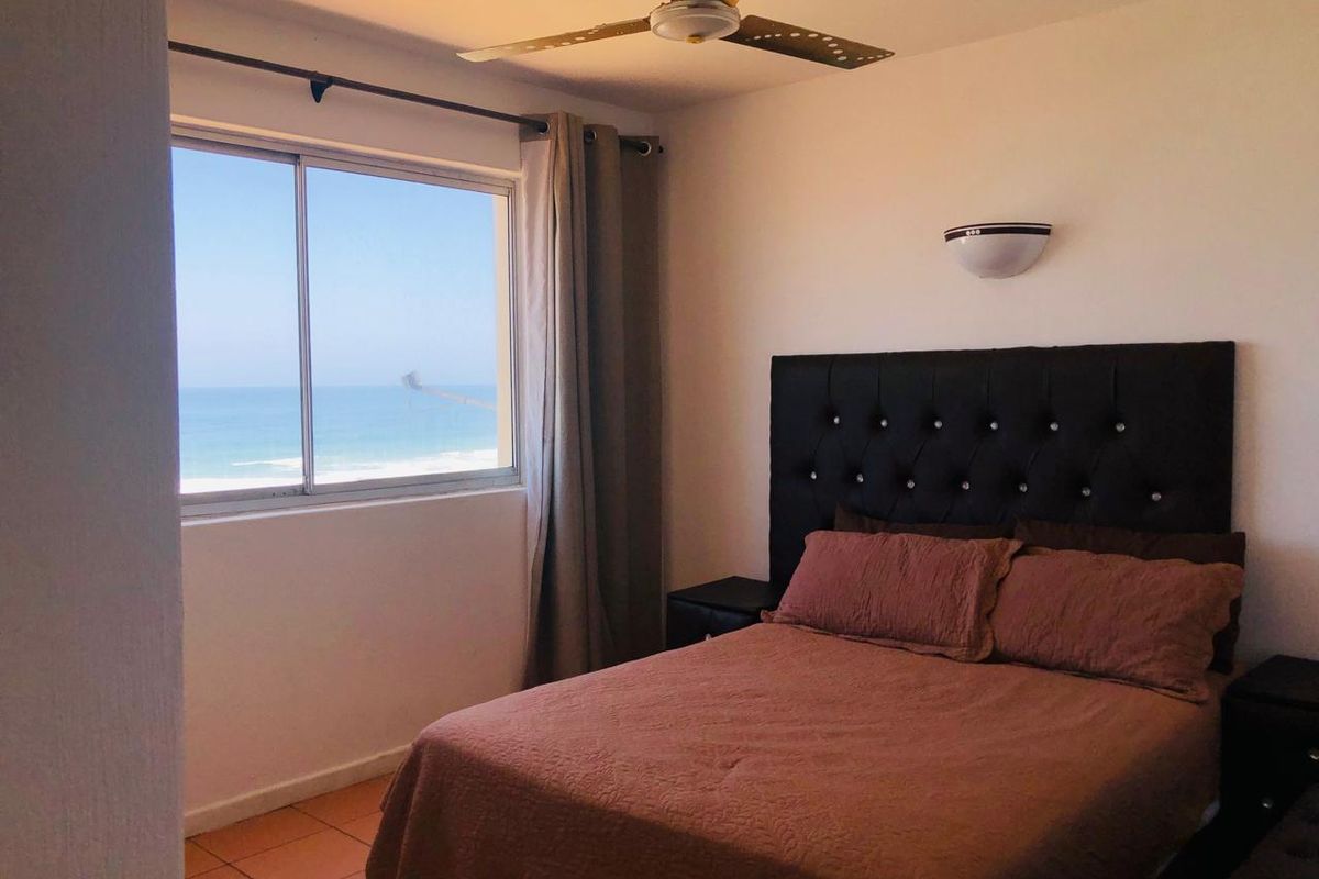A bedroom featuring tiled flooring, a ceiling fan, and a sliding window offering a direct ocean view.