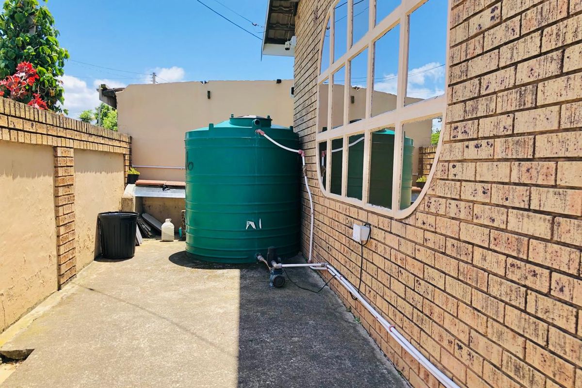 Rear exterior area featuring a water storage tank with pump, concrete paving, and brick boundary wall.