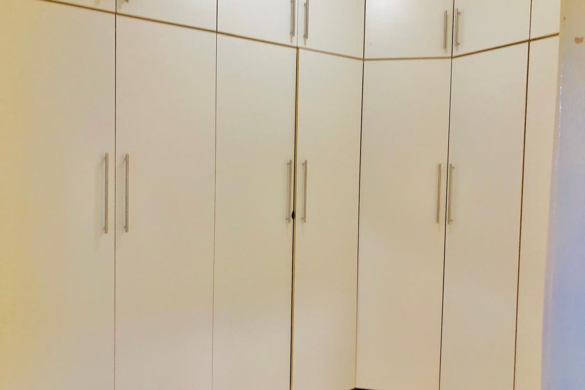 A bedroom featuring extensive floor-to-ceiling built-in cupboards with modern handles, providing ample storage space.