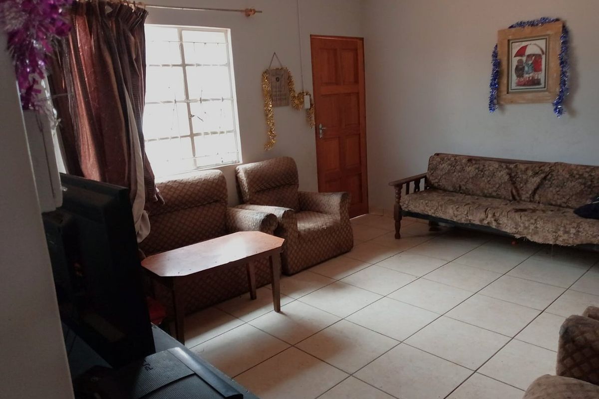 A living room featuring tiled flooring, a timber door, and a window fitted with security bars.