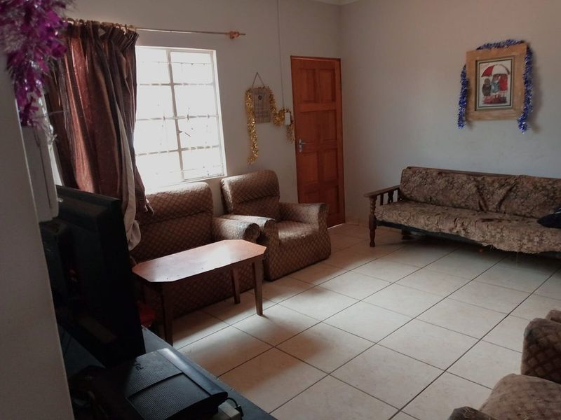 A living room featuring tiled flooring, a timber door, and a window fitted with security bars.