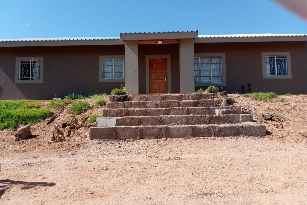 Front elevation of a single-story house featuring a covered entrance, timber door, security-barred windows, and unfinished concrete block steps leading to the main entry.