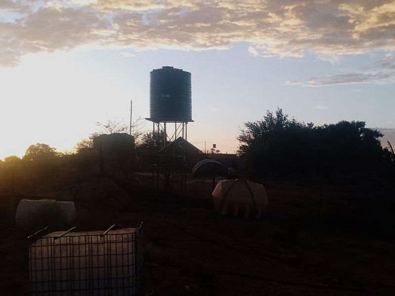 Outdoor area featuring a raised water storage tank on a metal stand, set against a sunset sky.