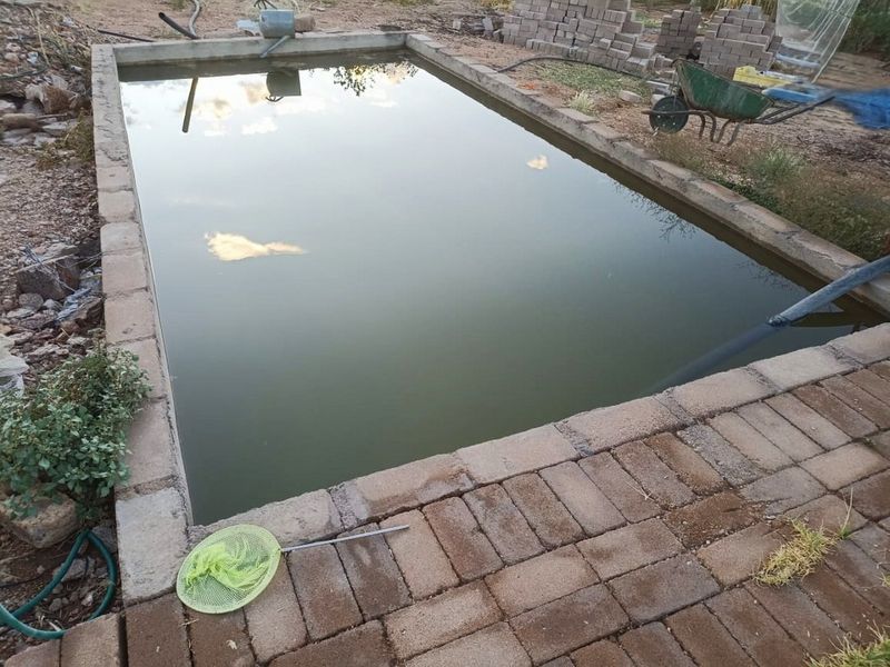 An outdoor swimming pool currently under construction with unfinished surrounding landscaping and paver coping.