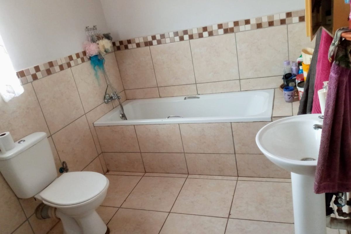 A functional bathroom featuring a bathtub, pedestal basin, and toilet with neutral ceramic wall and floor tiling.
