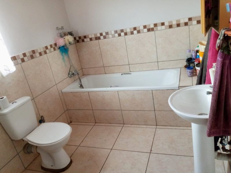 A functional bathroom featuring a bathtub, pedestal basin, and toilet with neutral ceramic wall and floor tiling.