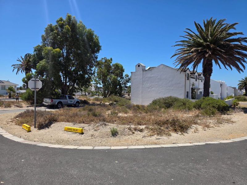 A street-level view of the property entrance and surrounding neighbourhood landscape, featuring paved road access and established vegetation.