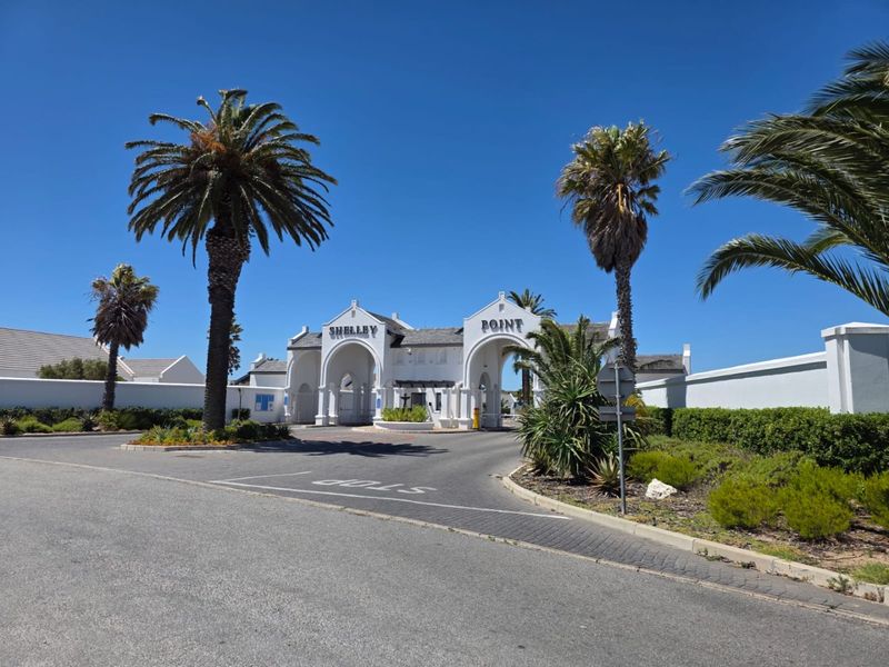 The main entrance gate and security access point for the Shelley Point estate, featuring white architectural arches and manicured landscaping.